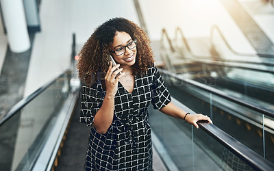 Buy stock photo High angle shot of an attractive young businesswoman taking a phonecall while going up an escalator in a modern office