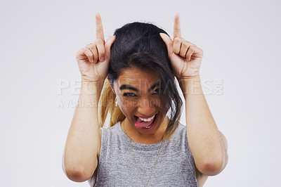 Buy stock photo Portrait, funny face and devil horns with a woman in studio on a gray background looking silly or goofy. Comedy, comic and playing with a crazy young female person joking for carefree fun or humor