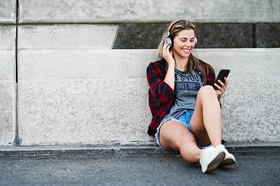 Buy stock photo Full length shot of an attractive young woman sitting down and listening to music on her cellphone in the city