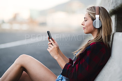 Buy stock photo Shot of an attractive young woman sitting down and listening to music on her cellphone in the city