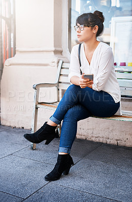 Buy stock photo Shot of a beautiful young woman seated on a bench while waiting for her ride