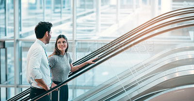 Buy stock photo Cropped shot of two young businesspeople having a chat while going up an escalator in a modern workplace