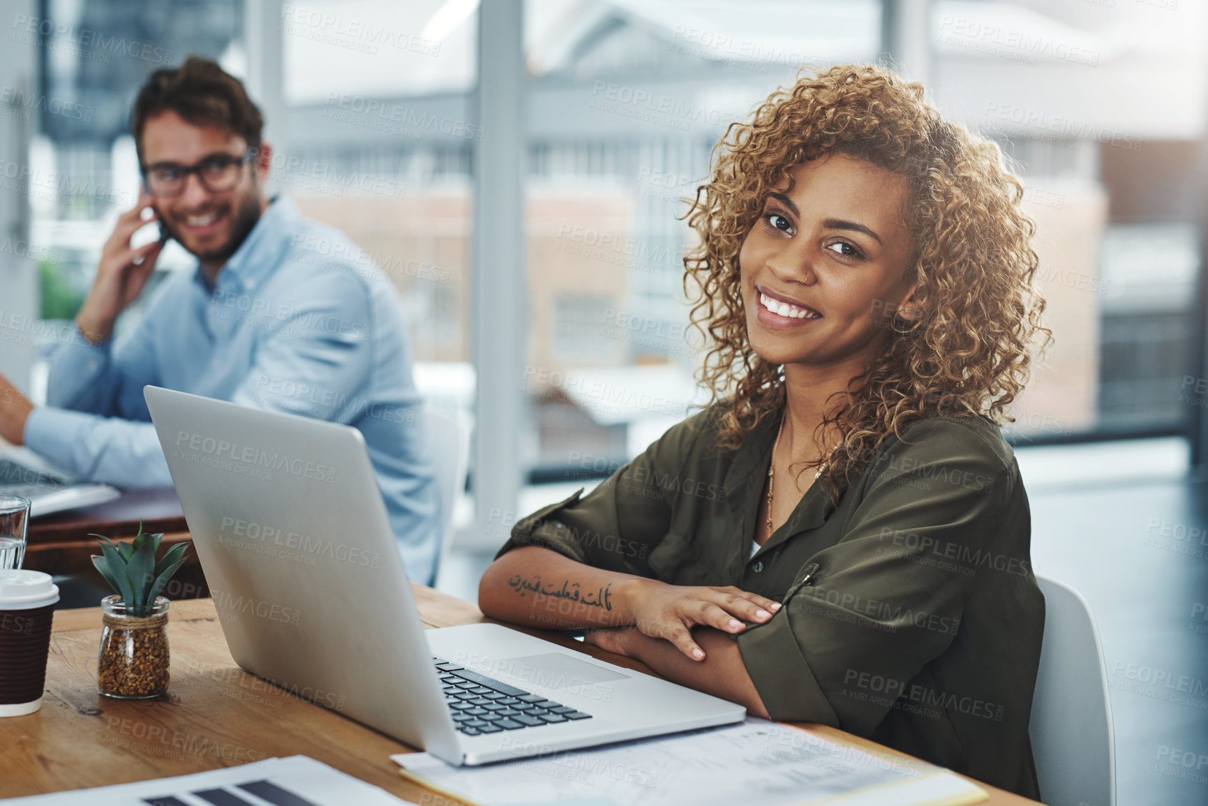 Buy stock photo Portrait of a young woman working at her desk with her colleague in the background