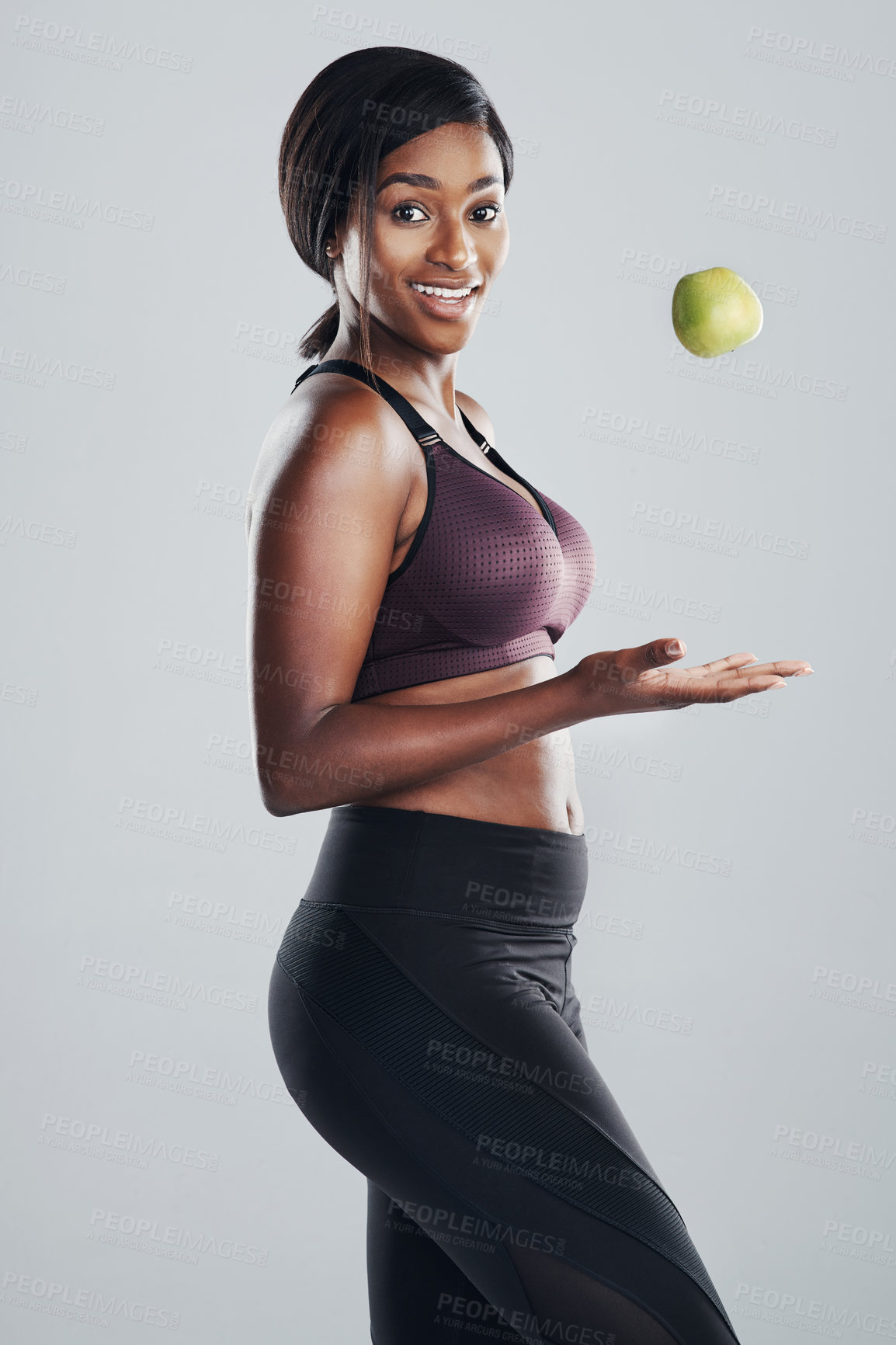 Buy stock photo Studio portrait of an attractive and fit young woman throwing an apple in the air against a grey background