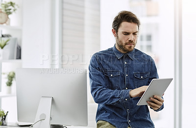Buy stock photo Cropped shot of a handsome young businessman using a digital tablet in his office