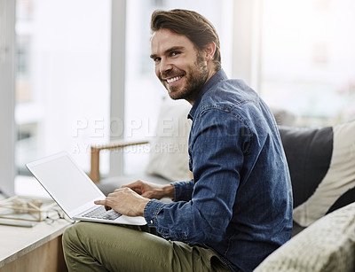 Buy stock photo Cropped portrait of a handsome young man smiling while using a laptop in his living room at home