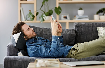Buy stock photo Cropped shot of a handsome young man using a smartphone while lying on a couch at home
