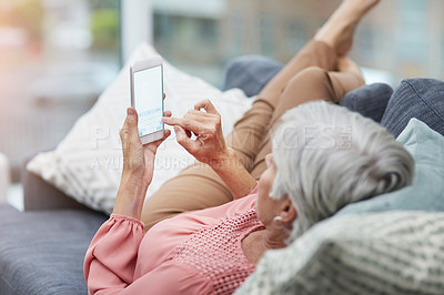 Buy stock photo High angle shot of a mature woman using her cellphone while relaxing on a sofa at home