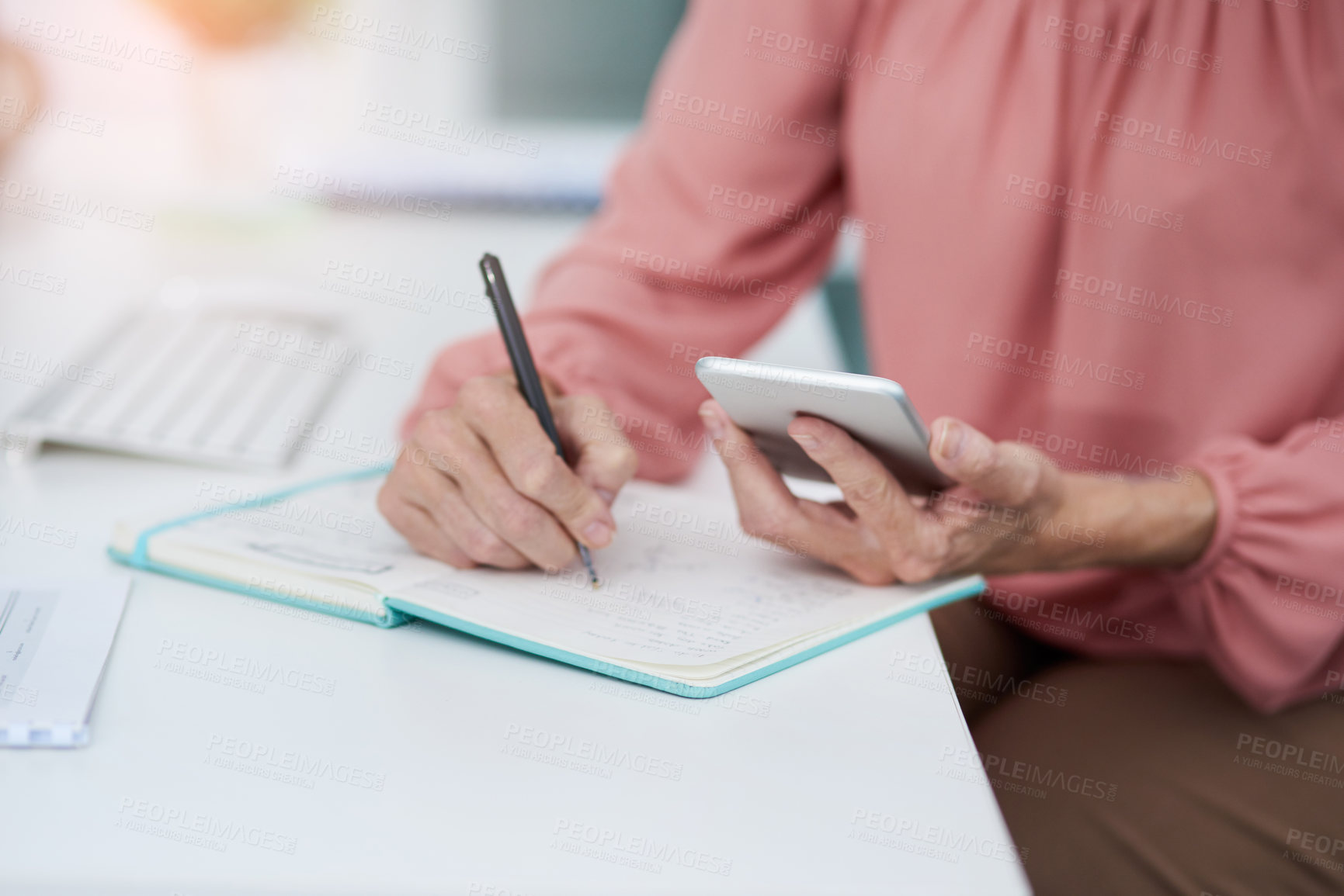 Buy stock photo Shot of an unrecognizable mature woman writing down details from her cellphone to her diary at work