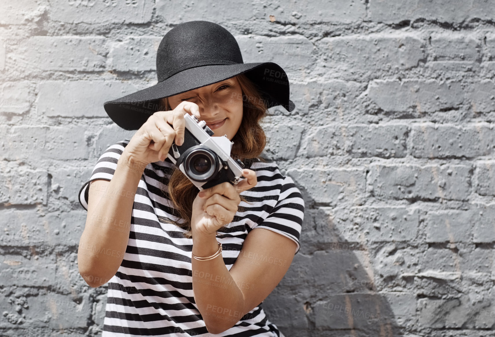 Buy stock photo Shot of a young woman taking a picture with her camera against a brick wall outdoors