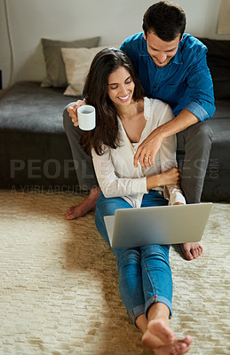 Buy stock photo Shot of a cheerful young couple using a laptop together while relaxing at home