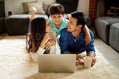 Buy stock photo Shot of a young couple and their son lying down on the carpet and using a laptop together at home