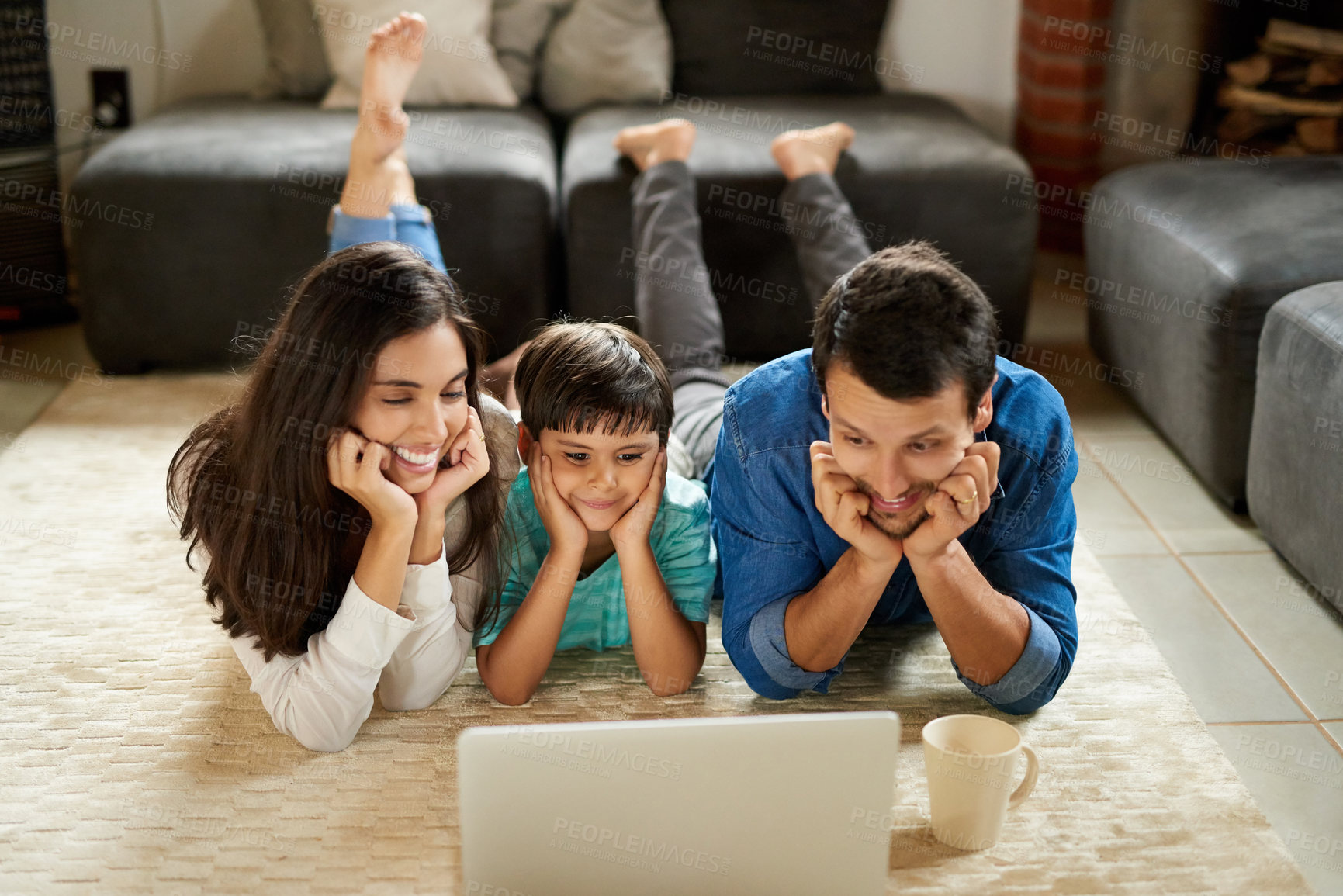 Buy stock photo Shot of a young couple and their son lying down on the carpet and using a laptop together at home