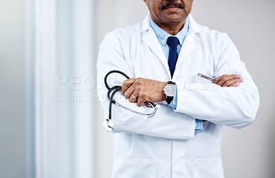 Buy stock photo Shot of an unrecognizable male doctor standing with his arms folded inside of a hospital during the day