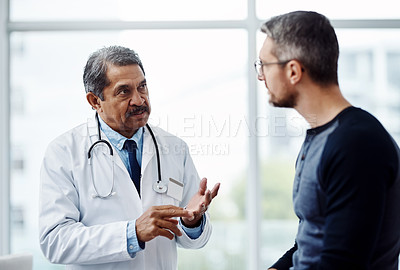 Buy stock photo Shot of a confident mature male doctor consulting a patient  inside a hospit