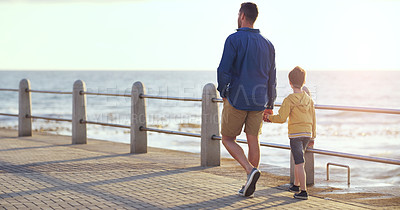 Buy stock photo Father, boy and holding hands on promenade, beach or walking on vacation with love, care and bonding. Man, child and outdoor together by sea, waves and back for holiday in summer sunshine with family