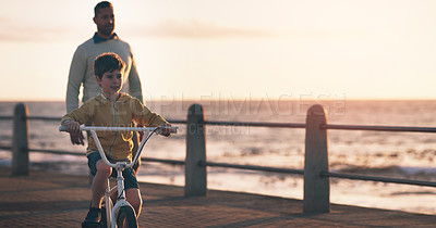 Buy stock photo Father, boy and bike for learning at beach, promenade and sunset on vacation with care, love and bonding. Man, child and bicycle with support, teaching and outdoor by sea, waves and holiday in summer
