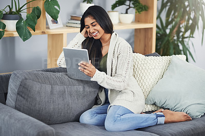 Buy stock photo Shot of a happy young woman using her digital tablet while relaxing on her couch at home