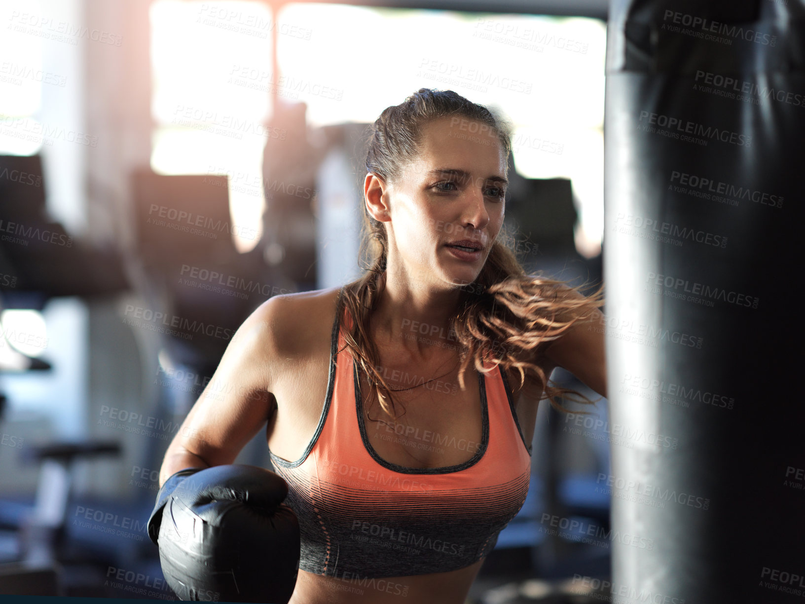 Buy stock photo Shot of a young female boxer working out on a punching bag in the gym