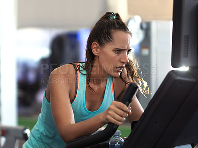Buy stock photo Shot of a determined looking young woman working out on an elliptical machine in the gym