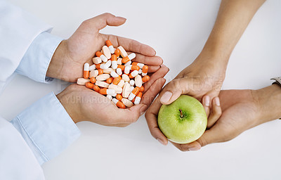 Buy stock photo Closeup shot of a medical practitioner holding a variety of pills while her colleague holds an apple in her hand