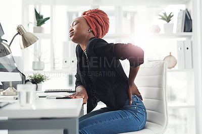 Buy stock photo Cropped shot of an attractive young businesswoman holding her back in pain while sitting at her desk in the office