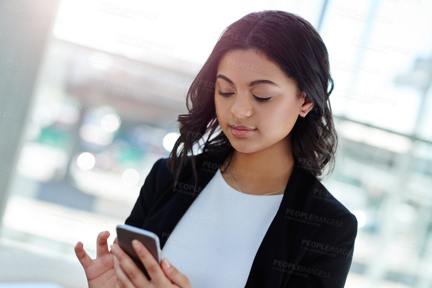 Buy stock photo Cropped shot of an attractive young businesswoman using a smartphone while standing in a modern office