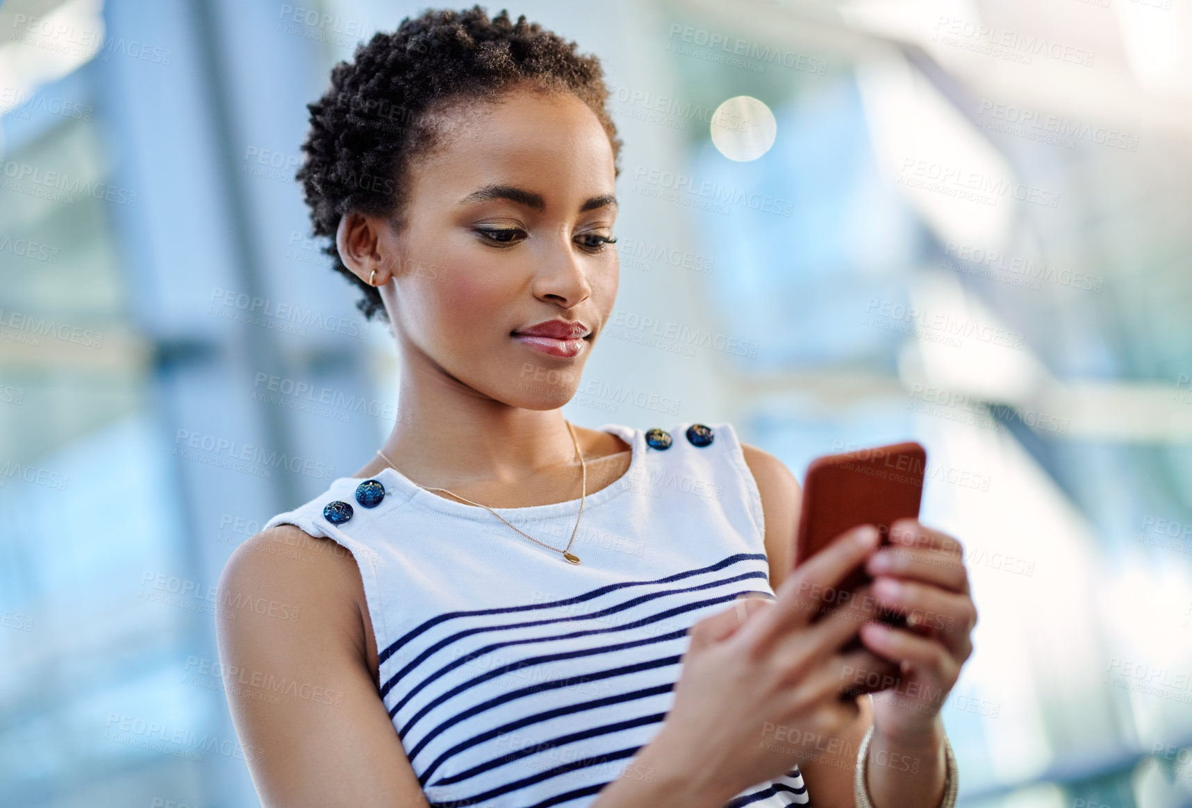Buy stock photo Cropped shot of an attractive young businesswoman using a smartphone while sitting in a modern workplace