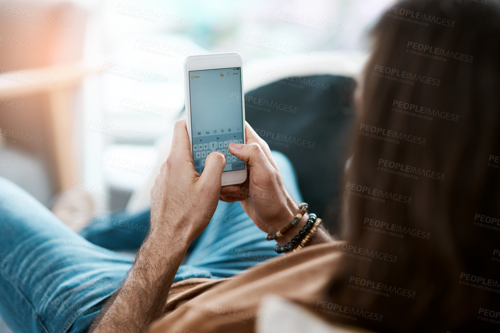 Buy stock photo Shot of a young man using his cellphone while relaxing on a sofa in his living room