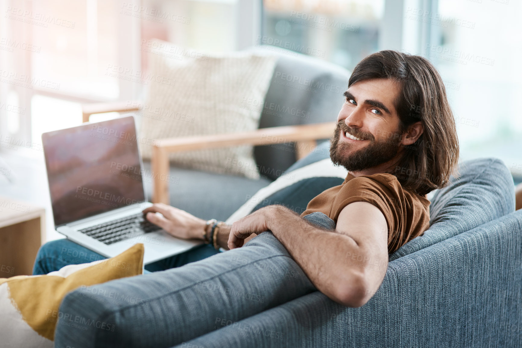 Buy stock photo Shot of a handsome young man using his laptop while relaxing on a sofa in his living room