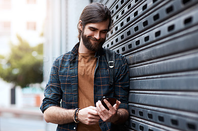 Buy stock photo Shot of a handsome young man using his cellphone while walking in the city