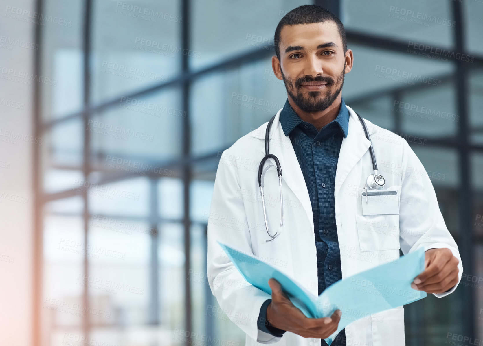 Buy stock photo Portrait of a young doctor going over the contents of a file in a modern hospital