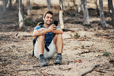 Buy stock photo Cropped shot of a cheerful young man texting on his cellphone while going for a hike up a mountain