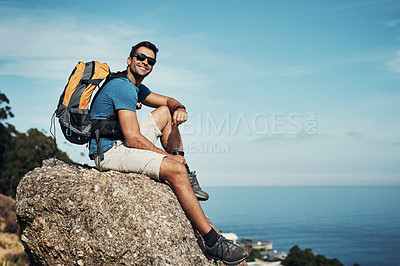 Buy stock photo Portrait of a carefree young man taking a quick break from hiking up a mountain during the day