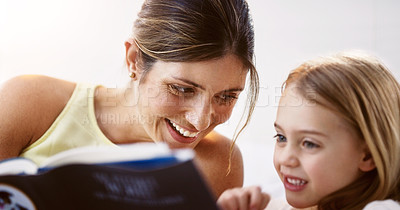 Buy stock photo Shot of a beautiful young mother reading a book with her daughter at home