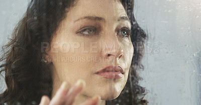 Buy stock photo Closeup shot of a sad young woman standing by a window while it's raining outside