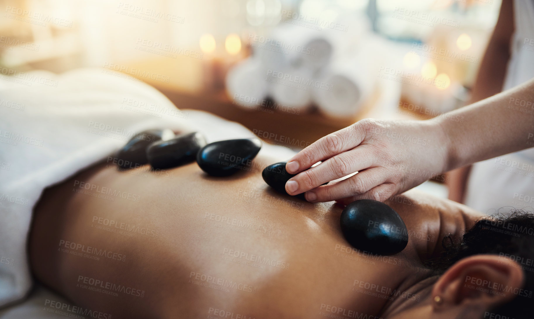 Buy stock photo Woman, hands and rocks in back massage at spa for skincare, beauty or relaxation on bed indoors. Hand of masseuse applying hot rock or stones on female for physical therapy or treatment at resort