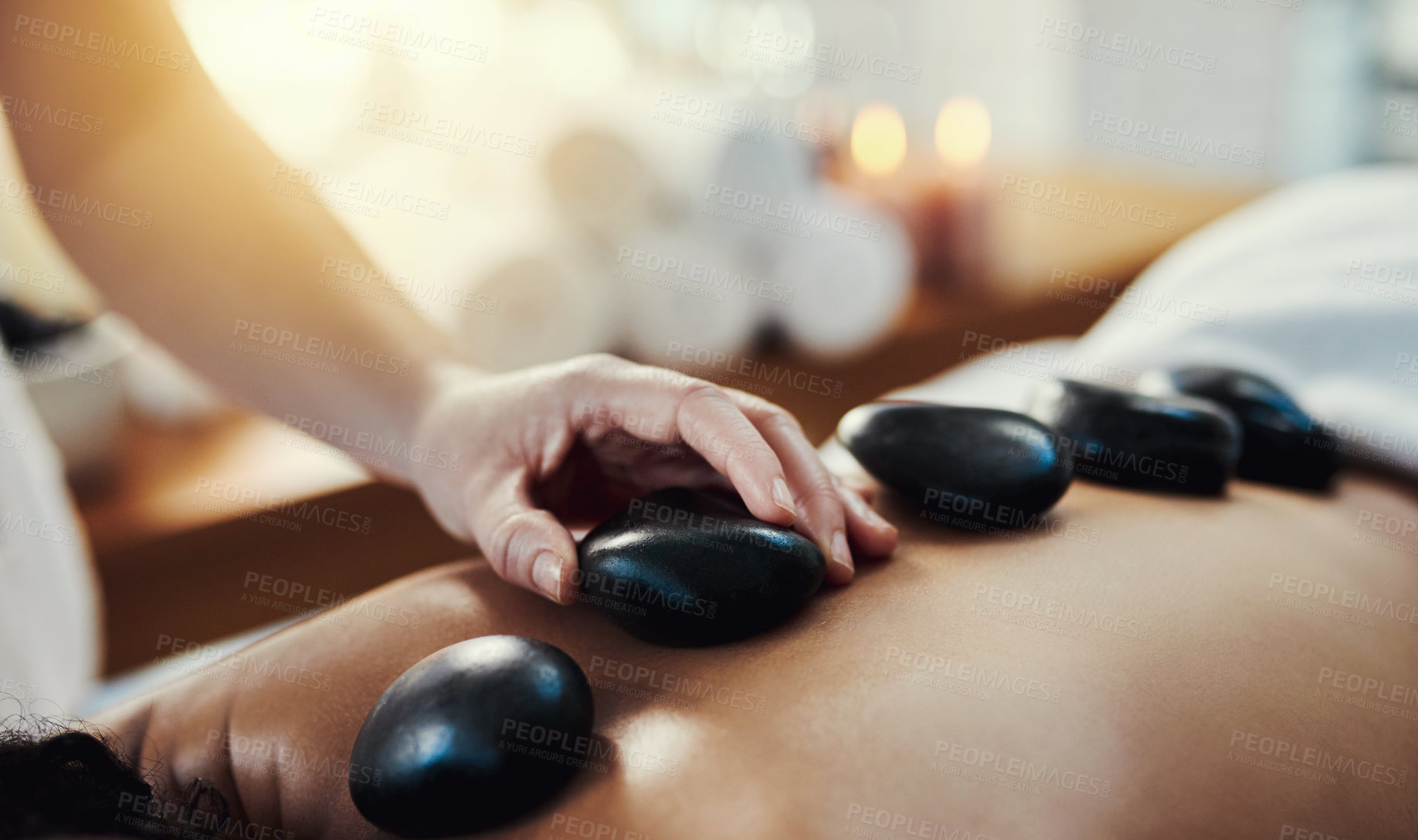 Buy stock photo Woman, hands and rocks in relax for back massage, skincare or beauty relaxation on bed at spa. Hand of masseuse applying hot rock or stones on female for physical therapy or treatment at a resort
