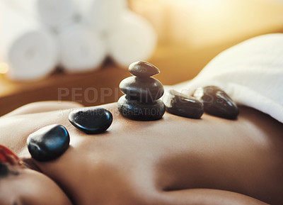 Buy stock photo Woman, hot rocks and massage on back at spa for skincare, beauty or body treatment at resort. Calm female lying on bed with heated rock pile for healthy physical therapy, zen or wellness at salon