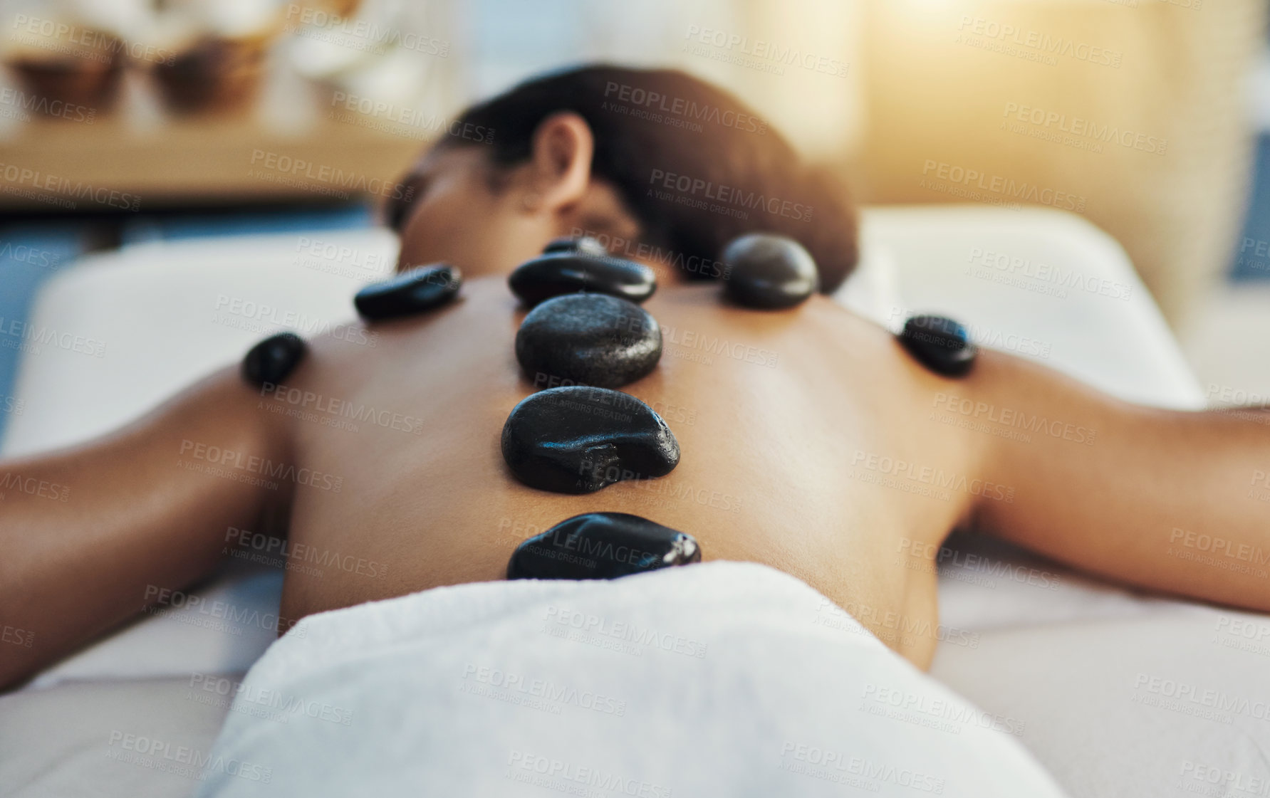 Buy stock photo Woman, relax and stone massage at spa for skincare, beauty or body treatment on bed at resort. Calm female lying in relaxation with hot rocks or pile on back in therapy, zen or wellness at salon