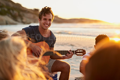 Buy stock photo Shot of a man playing the guitar while sitting on the beach with his friends