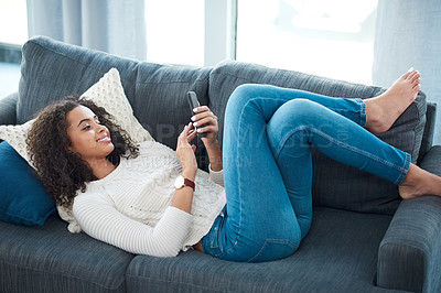 Buy stock photo Shot of a young woman using her cellphone while relaxing at home