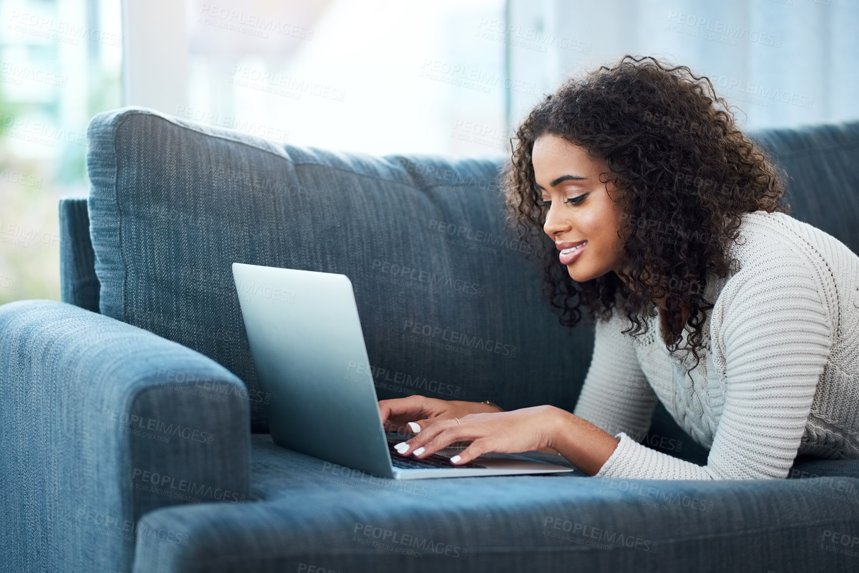 Buy stock photo Shot of a young woman using her laptop while relaxing at home