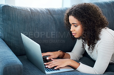 Buy stock photo Shot of a young woman using her laptop while relaxing at home