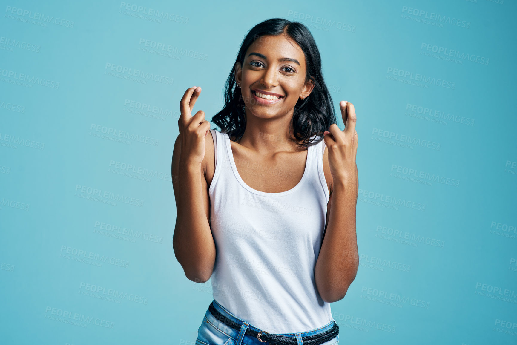 Buy stock photo Smile, fingers crossed and portrait of woman in studio for optimism, wish or good luck emoji. Happy, pride and Indian female person with hope hand gesture for superstition isolated by blue background