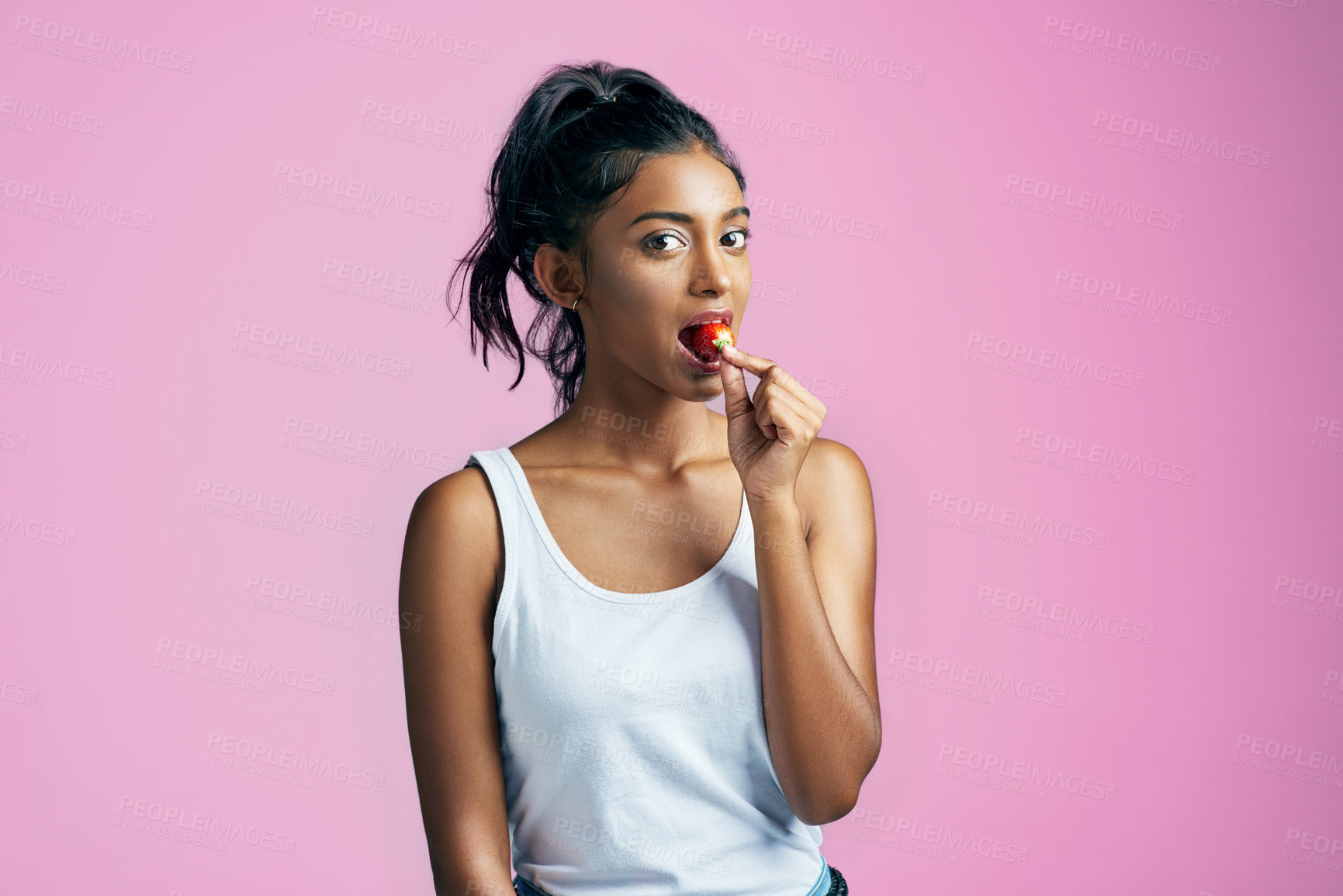 Buy stock photo Studio portrait of a beautiful young woman eating a strawberry against a pink background