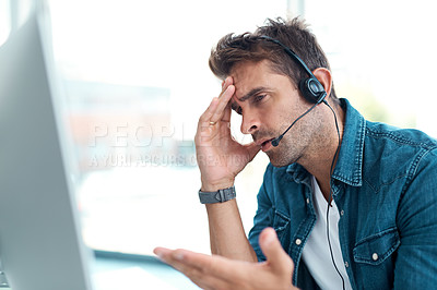 Buy stock photo Shot of a young call centre agent looking upset while working in his office
