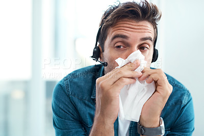Buy stock photo Shot of a male call centre agent blowing his nose with a tissue in his office
