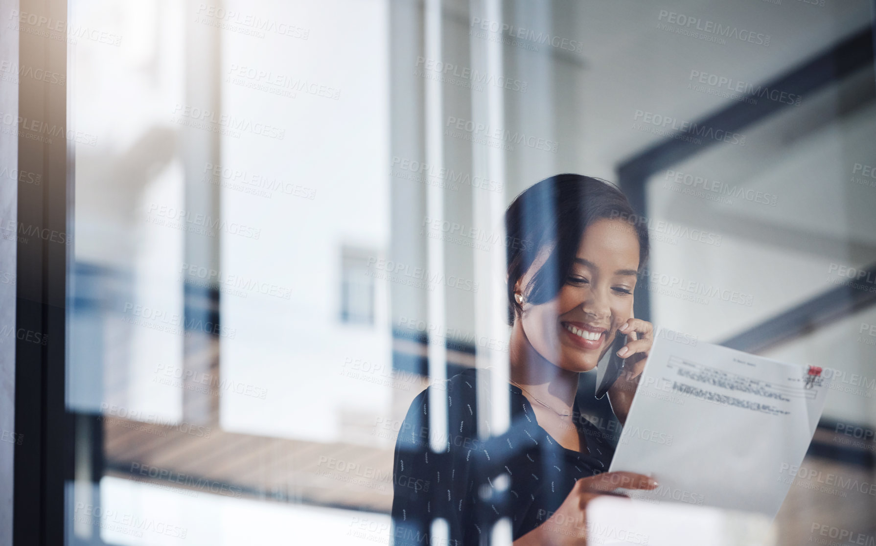 Buy stock photo Shot of a young businesswoman talking on a cellphone while going through paperwork in an office