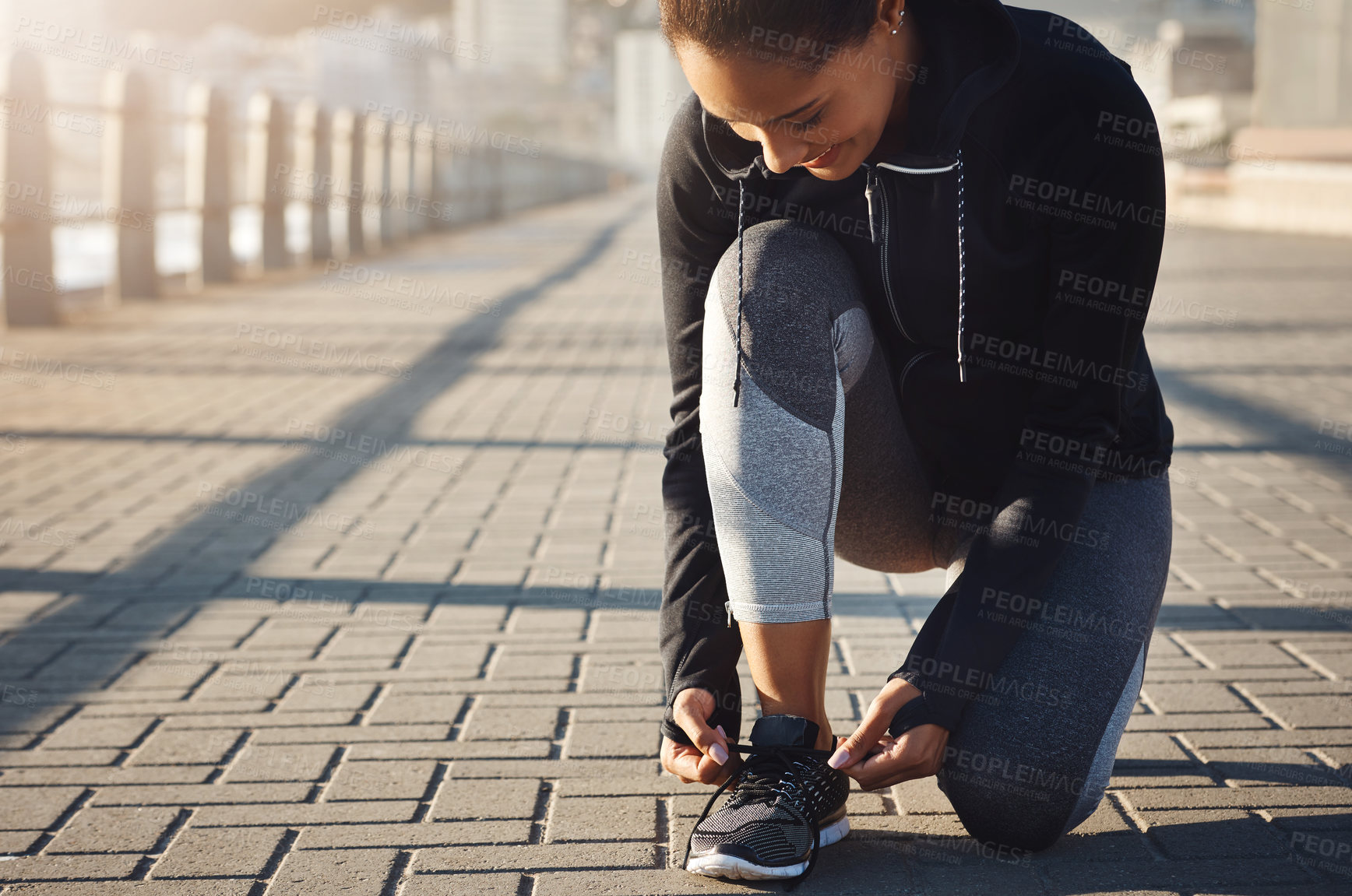 Buy stock photo Shot of a fit young woman tying her shoelaces before going for a run on the promenade